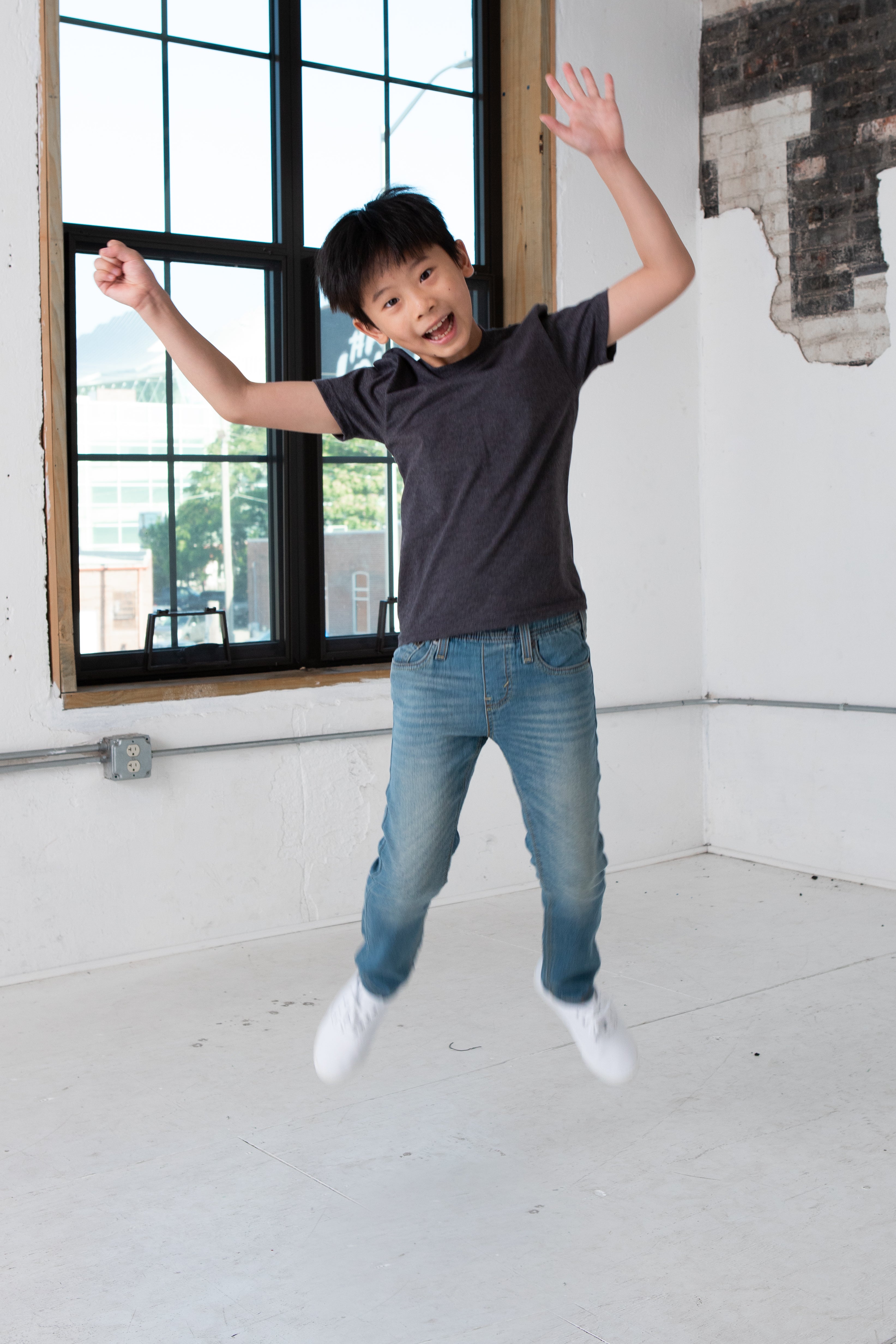 Boy Model wearing GOEX Youth Eco Triblend Tee in Charcoal and Jumping